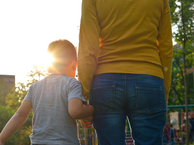 The back of a child and mother walking together and holding hands 