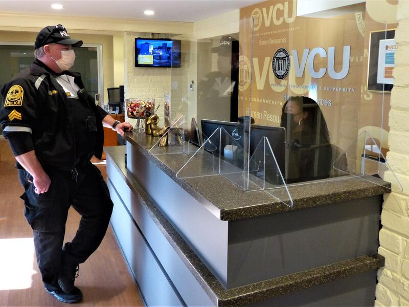 VCU police officer stands in front of reception desk speaking with woman sitting at the desk.