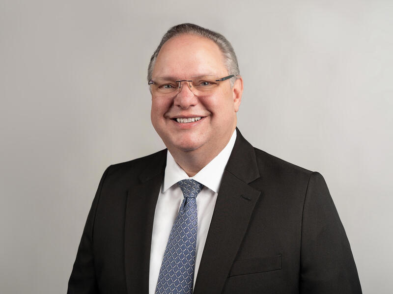 A man wearing glasses and a coat and tie, smiling.