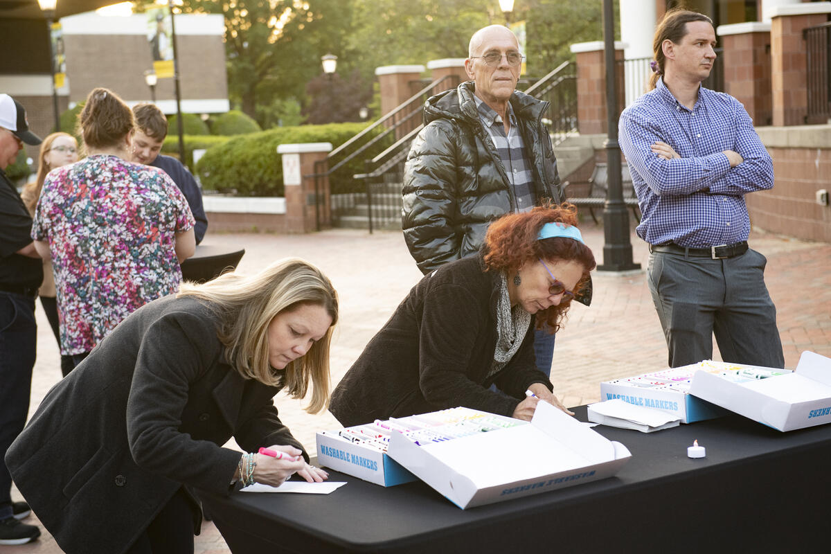 Two women are leaning over a table writing on pieces of paper. 