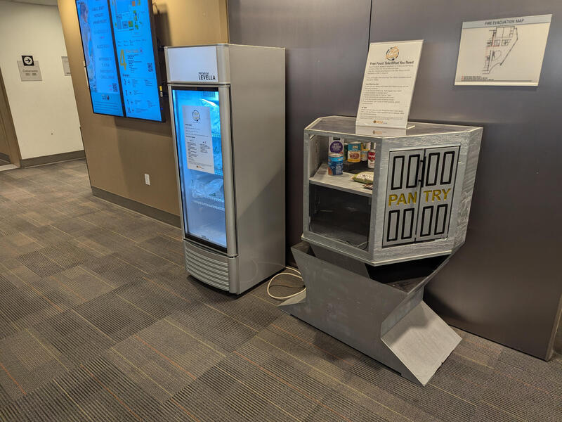 A small refrigerator sits against a wall alongside a small pantry with food in it.