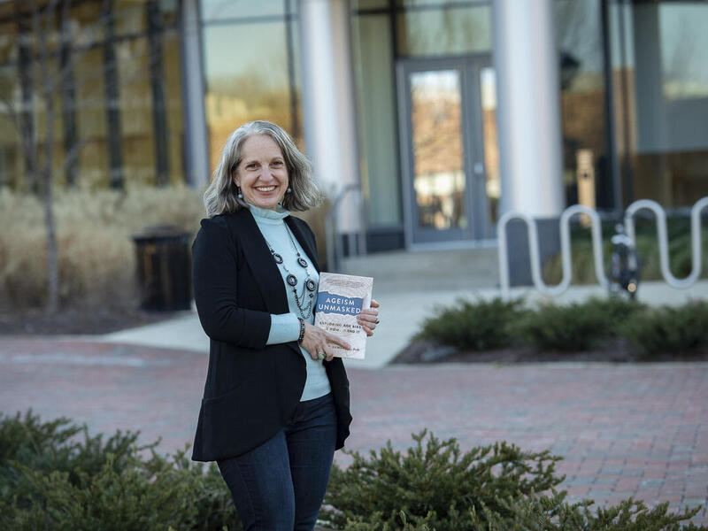 Tracey Gendron, Ph.D., director of the Virginia Center on Aging at VCU, holding her new book \"Ageism Unmasked: Exploring Age Bias and How to End It\" in front of Cabell Library 