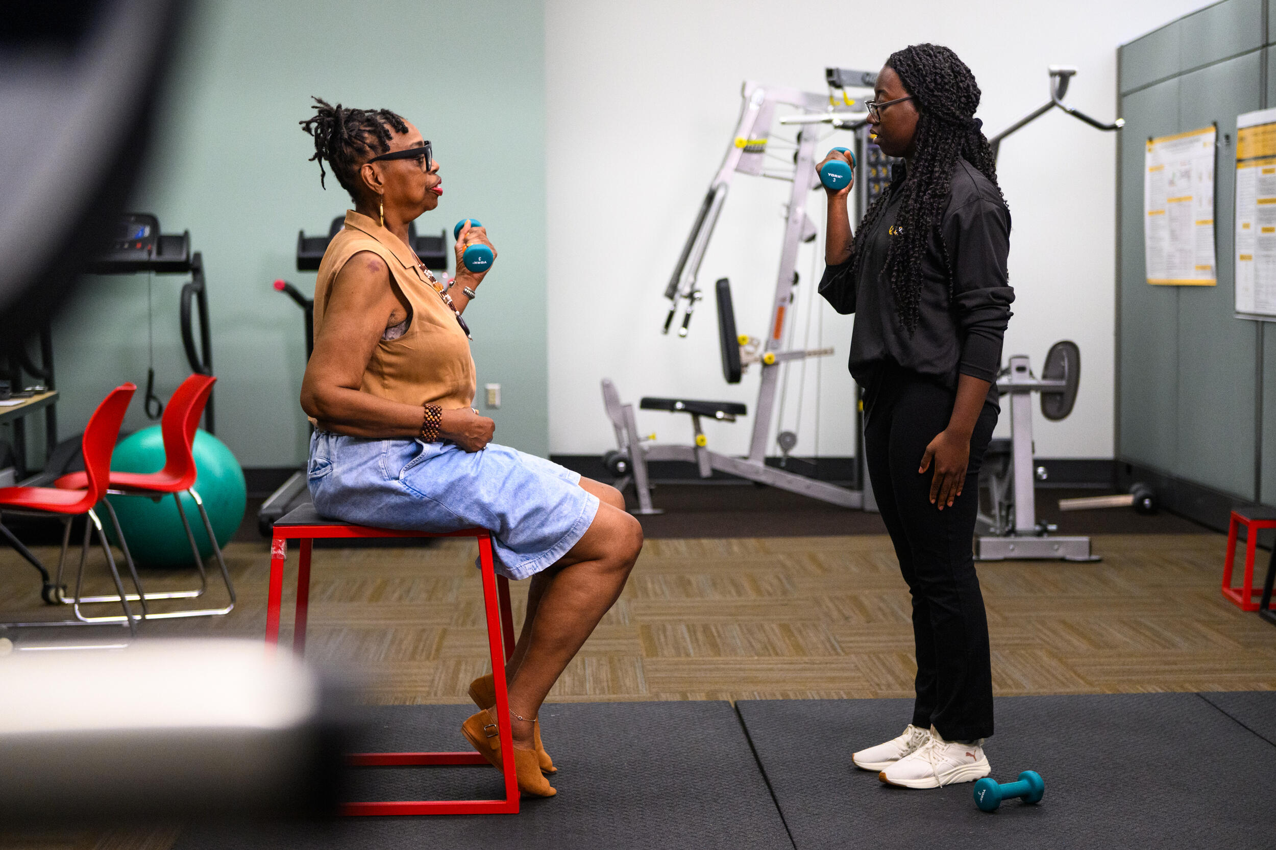 A photo of a woman sitting on a chair in front of a physical therapist who is holding a weight. 
