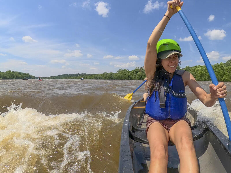 A photo of a woman canoeing in white water on a river. 