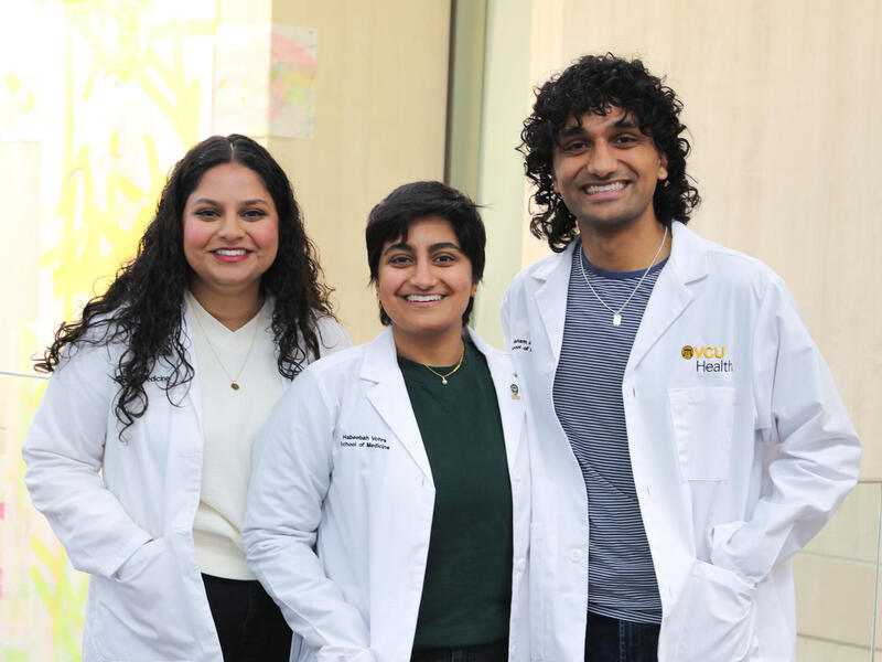 A photo of three people wearing whie lab coats and smiling. 