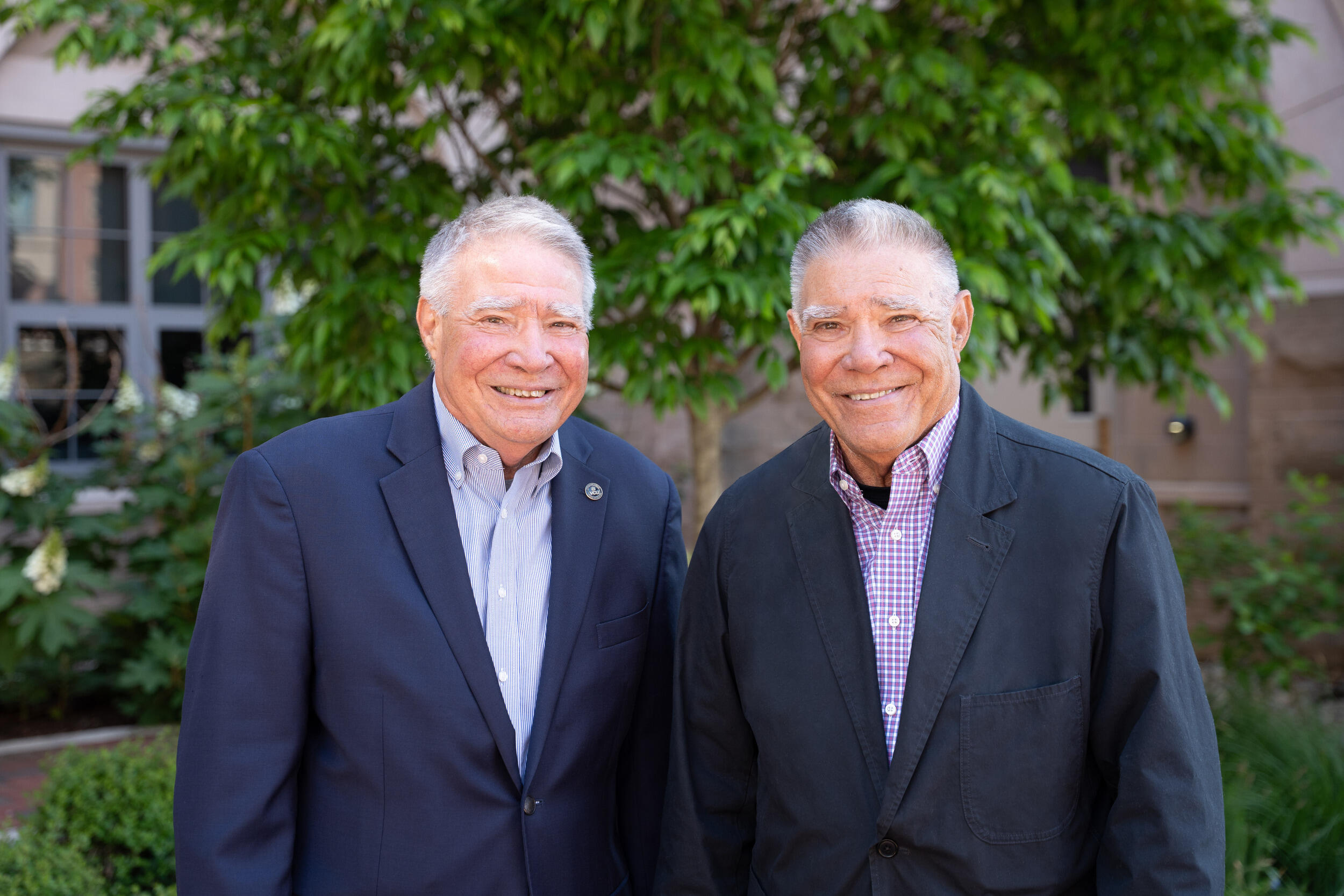 A photo of two men from the chest up who are standing outside an d smiling. 
