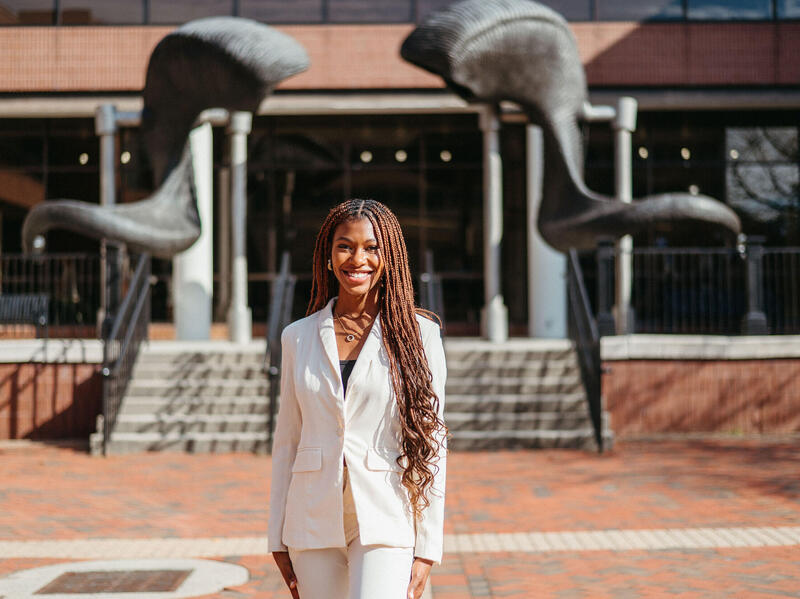 A woman wearing a white two piece suit standing in front of a ram horns statue. 