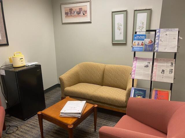 A room with a loveseat, mini fridge, small table, and arm chair. 