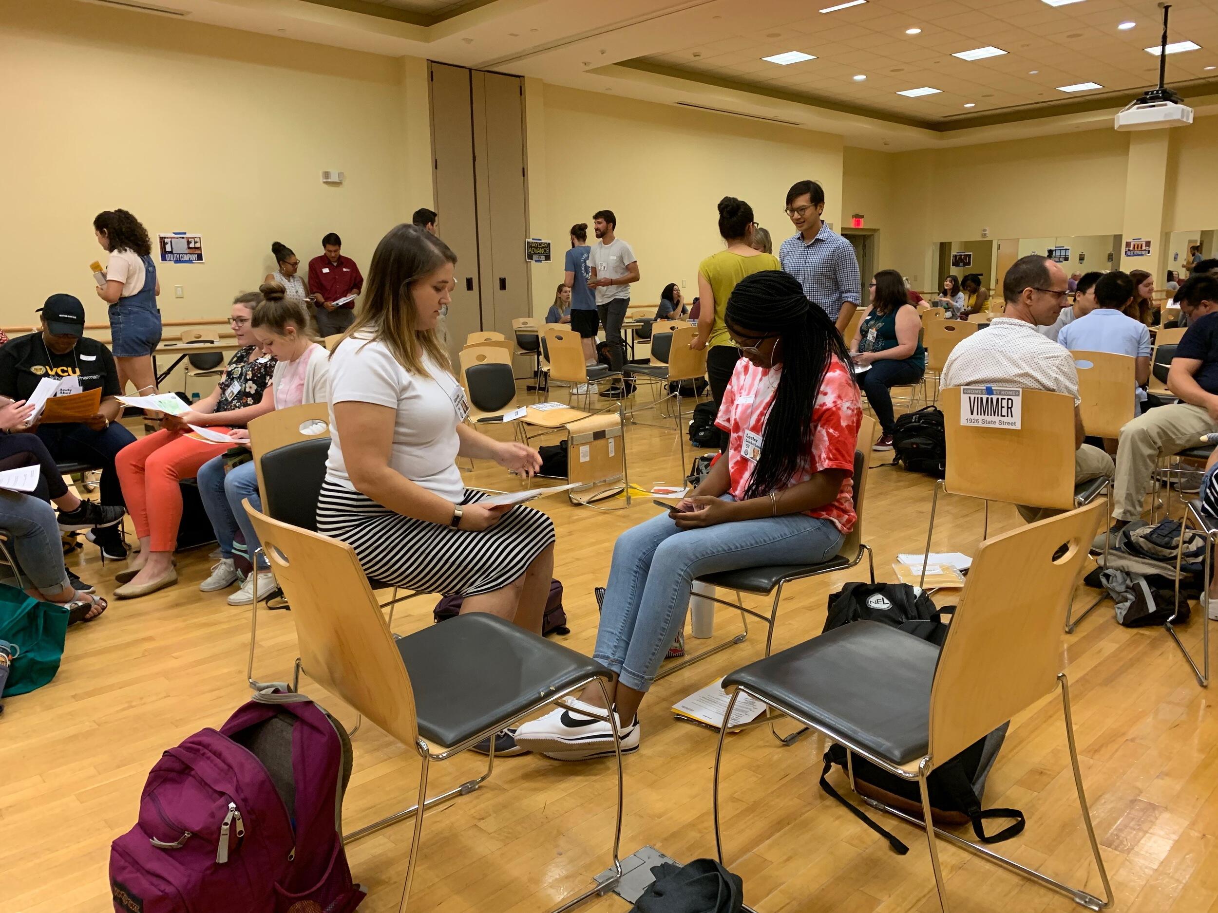 A group of people inside a large room participating in a poverty exercise.