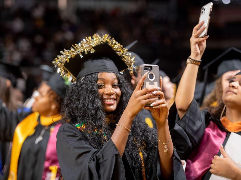 A new graduate in cap and gown smiles at the camera.
