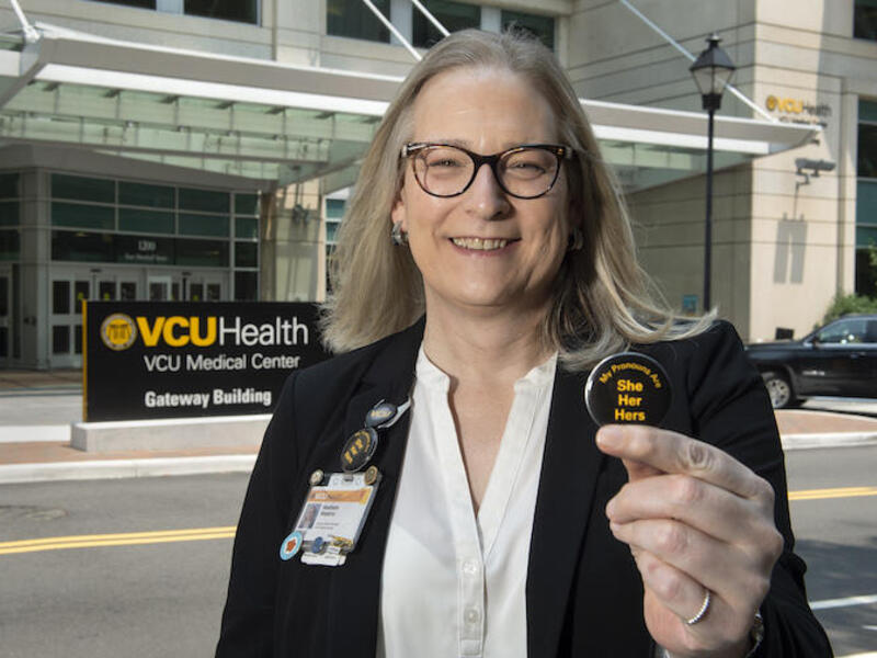 A woman holding a button that says \"she her hers\"