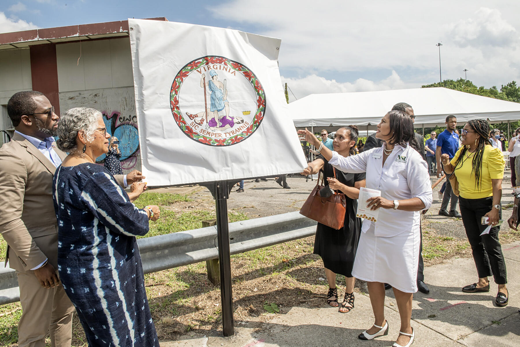 People standing around a sign covered with the symbol for the Commonwealth of Virginia 
