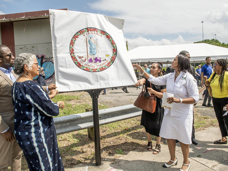 People standing around a sign covered with the symbol for the Commonwealth of Virginia 