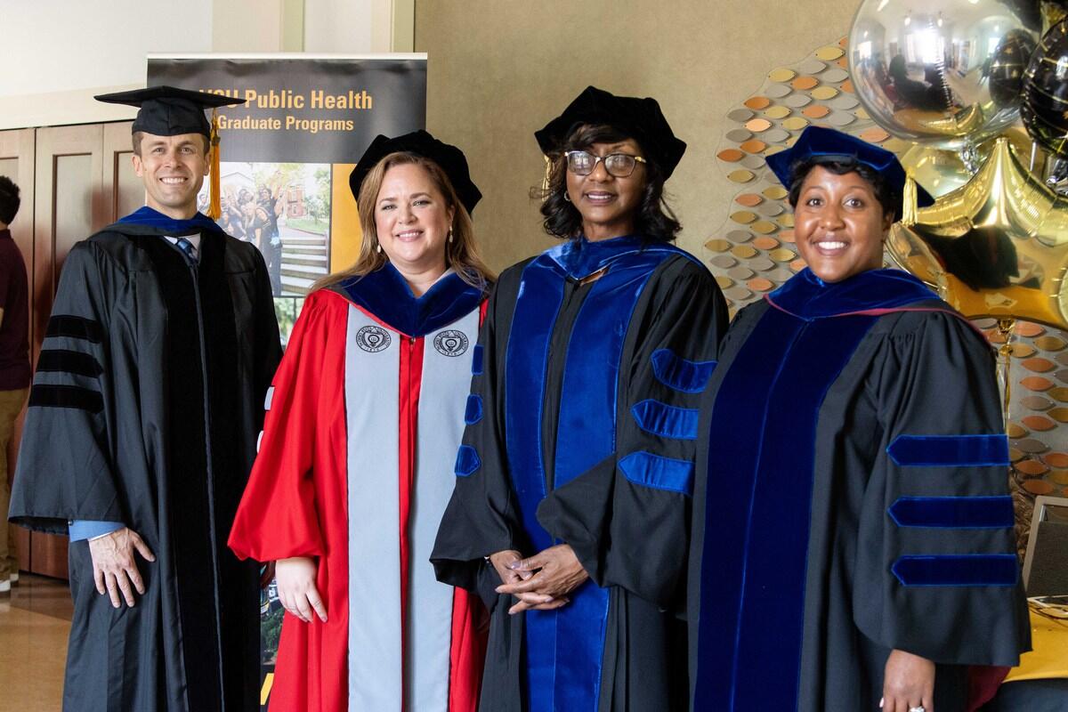 A group photo of four people wearing doctorate graduation cap and gowns. 