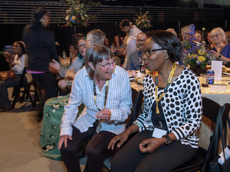 A photo of two women sitting next to each other at a circular table. 