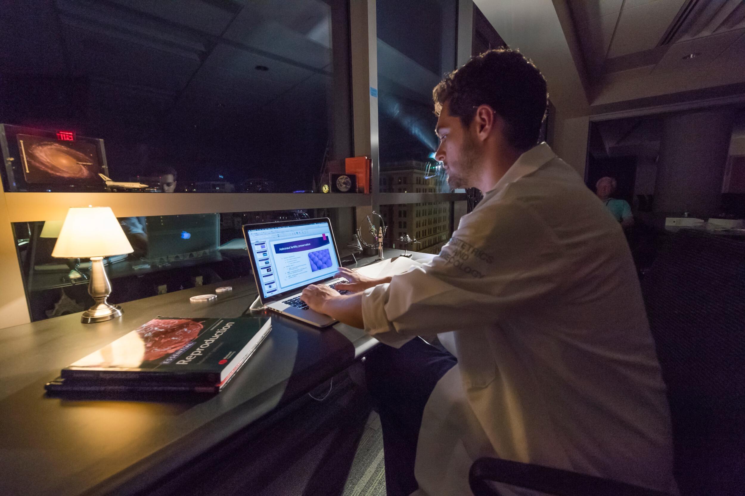 A photo of a man sitting at a table with a laptop in front of him. 