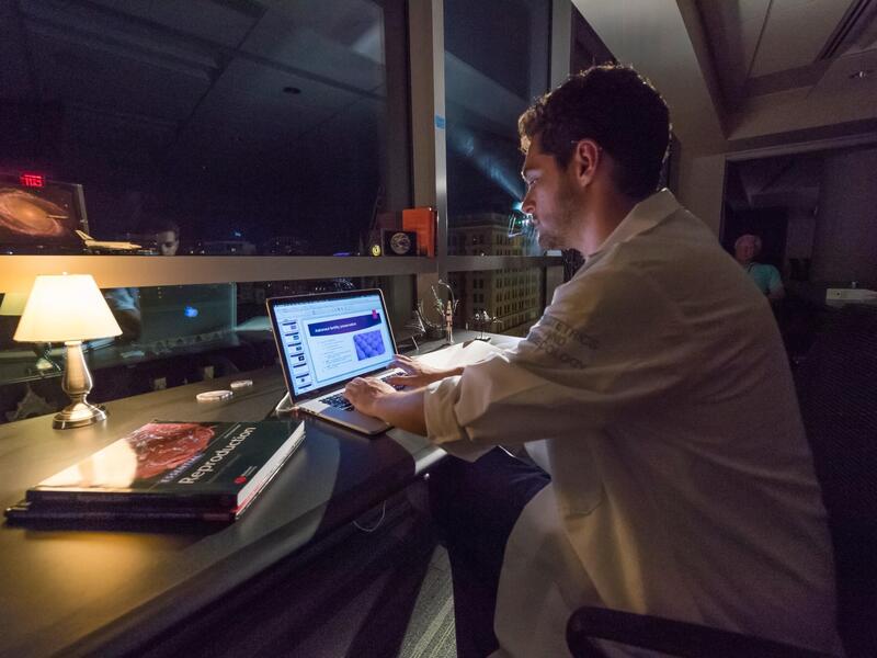 A photo of a man sitting at a table with a laptop in front of him. 