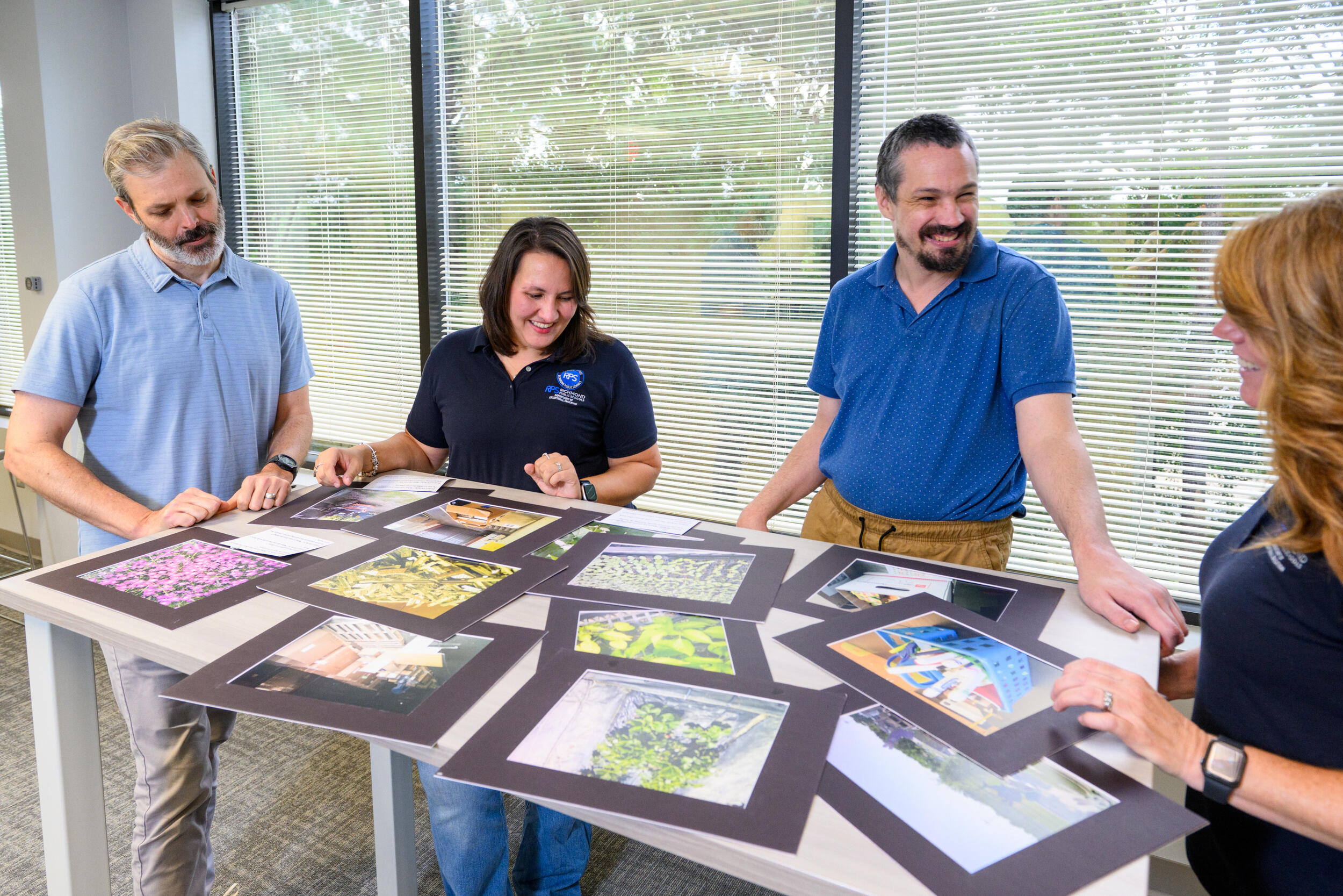 A photo of four people who are looking at photos that are covering a table. 