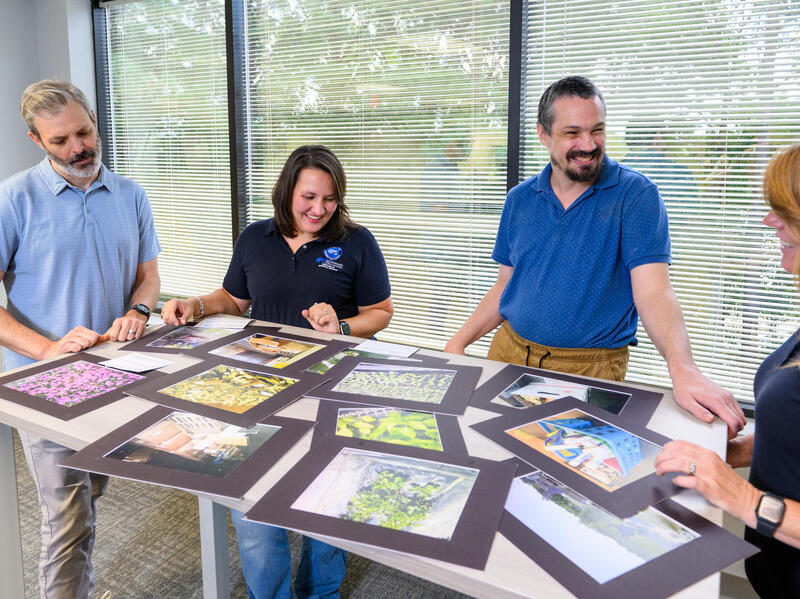 A photo of four people who are looking at photos that are covering a table. 