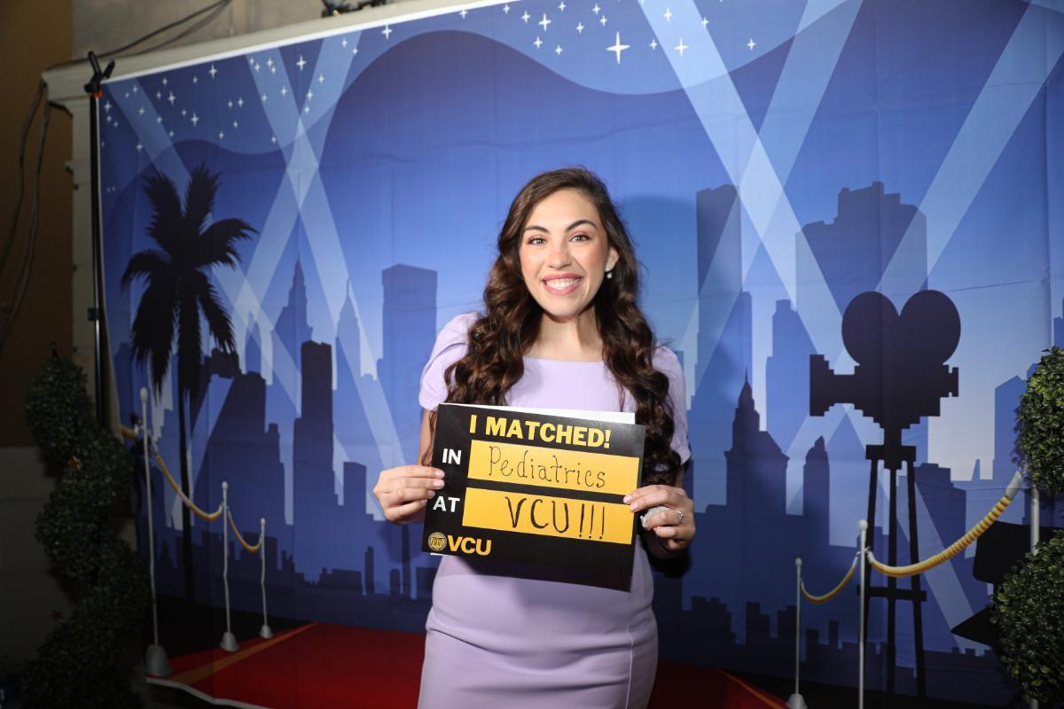 A photo of a woman holding a black and yellow sign that reads \"I MATCHED! IN Pediatrics AT VCU III.\" At the bottom of the sign is the VCU logo. 