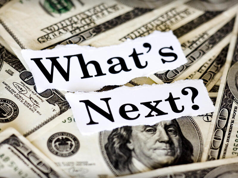 The words \"What's Next?\" in black text on white paper on top of hundred dollar bills 