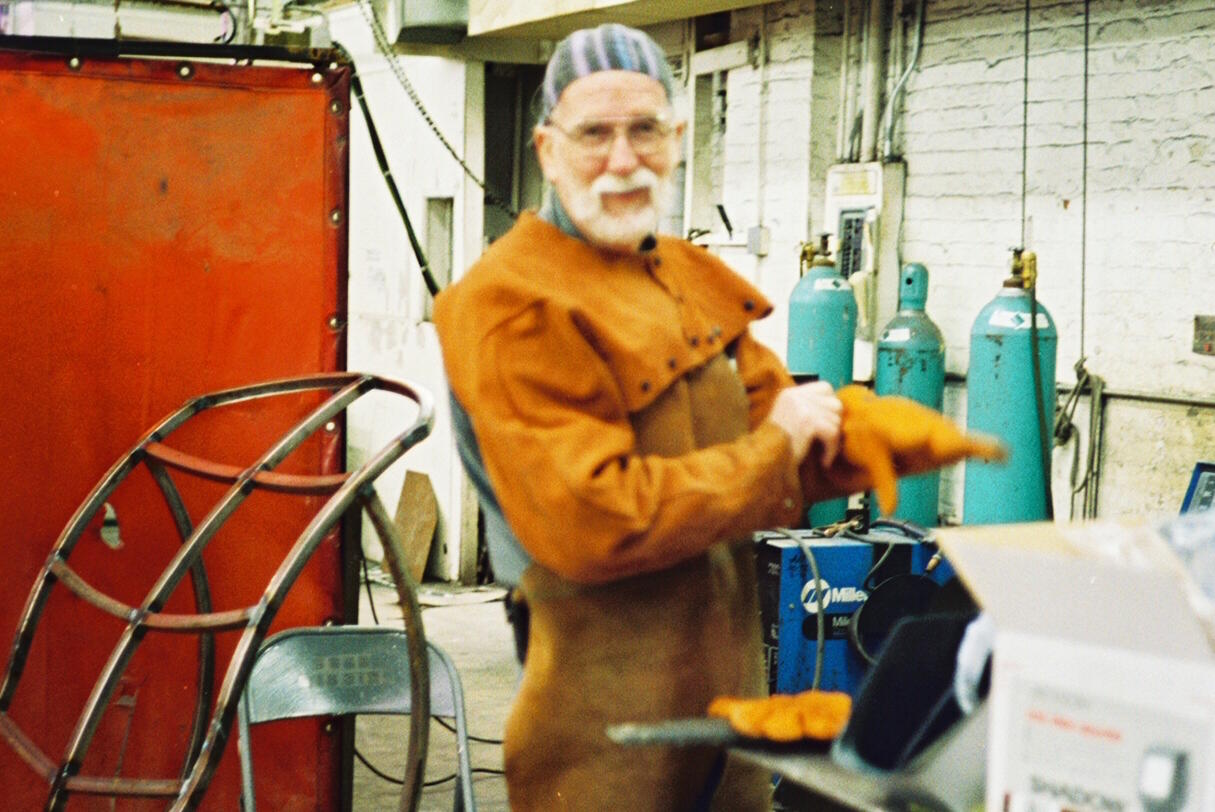Man in welding clothes stands in a studio.