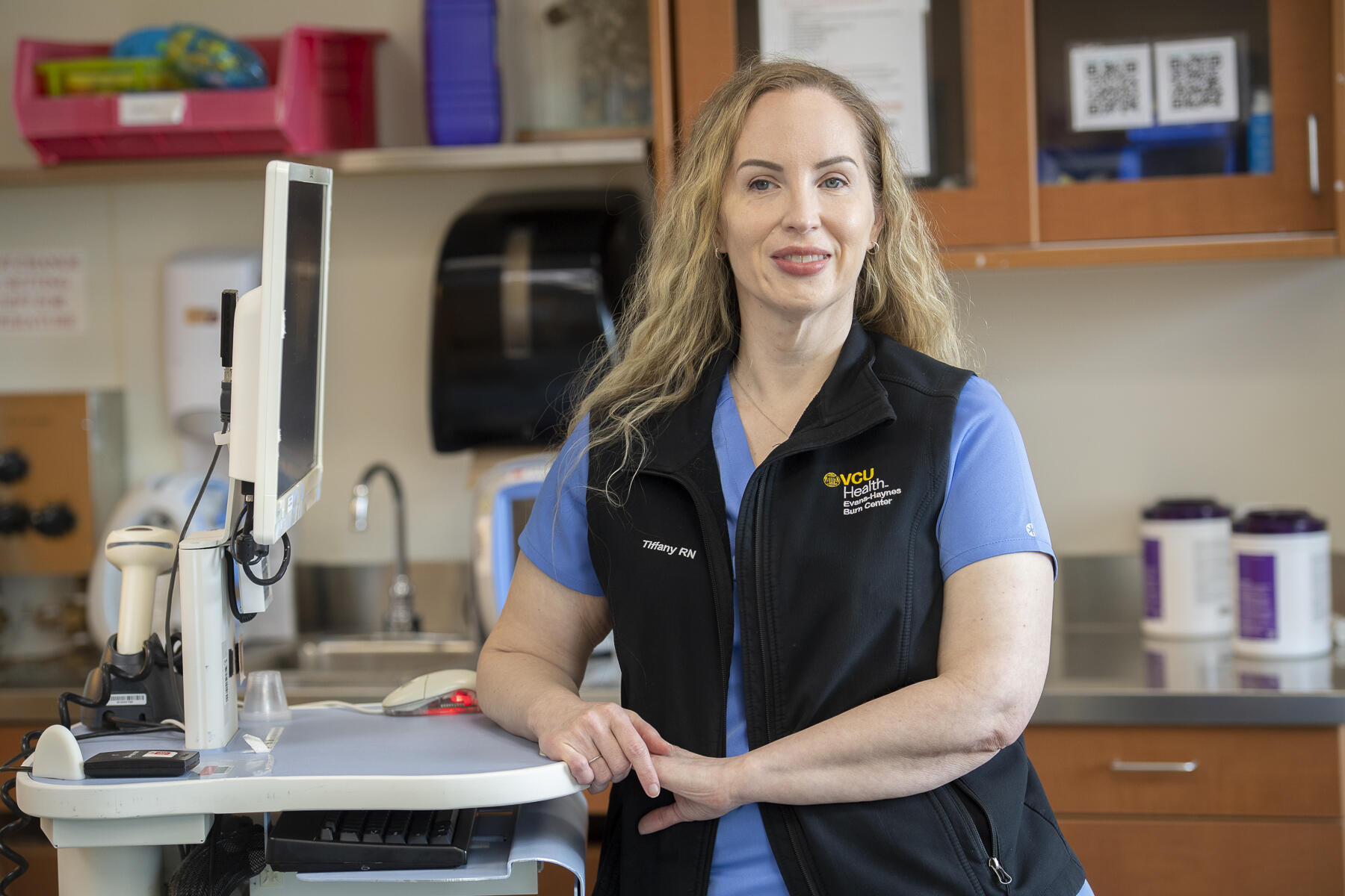 Tiffany Lord standing and leaning on desk next to computer screen.