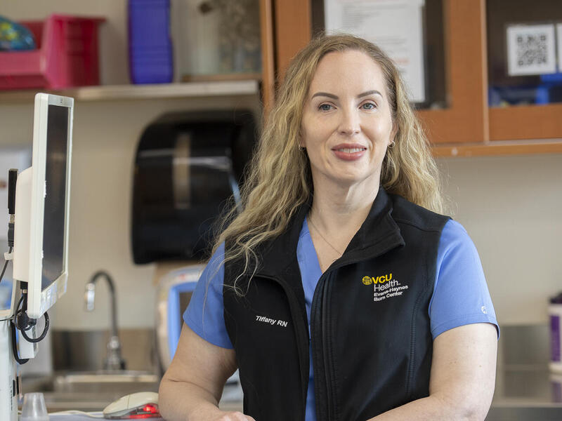 Tiffany Lord standing and leaning on desk next to computer screen.