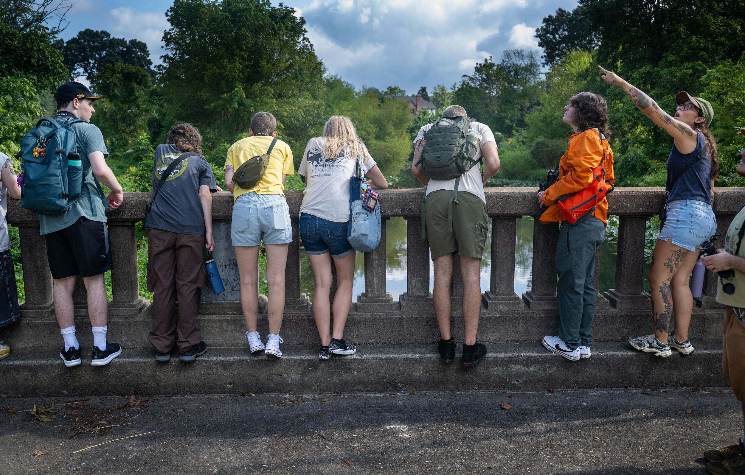 A photo of eight people standing at the edge of a bridge overlooking a river and forest. 