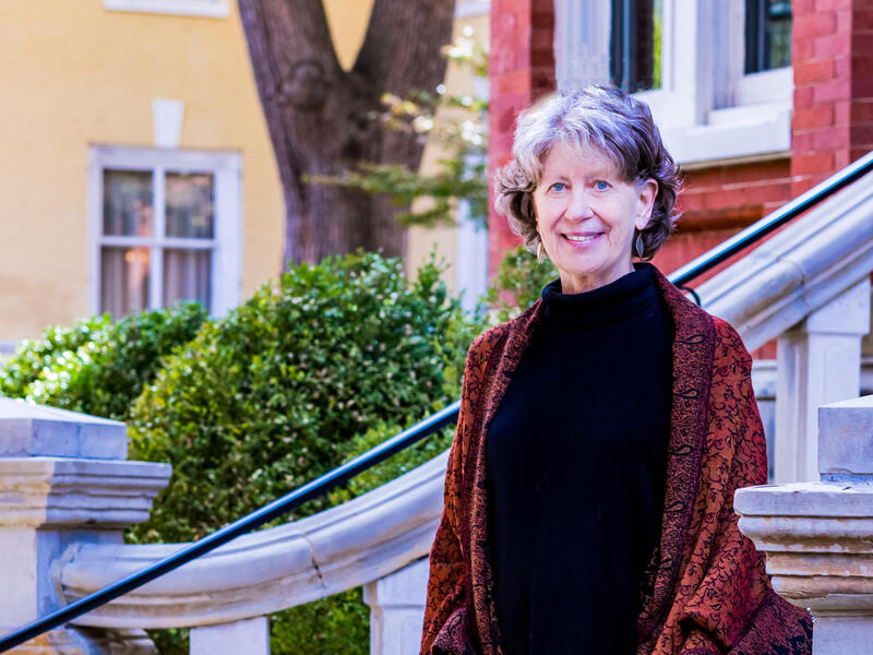A photo of a woman from the waist up. She is standing on a staircase. 
