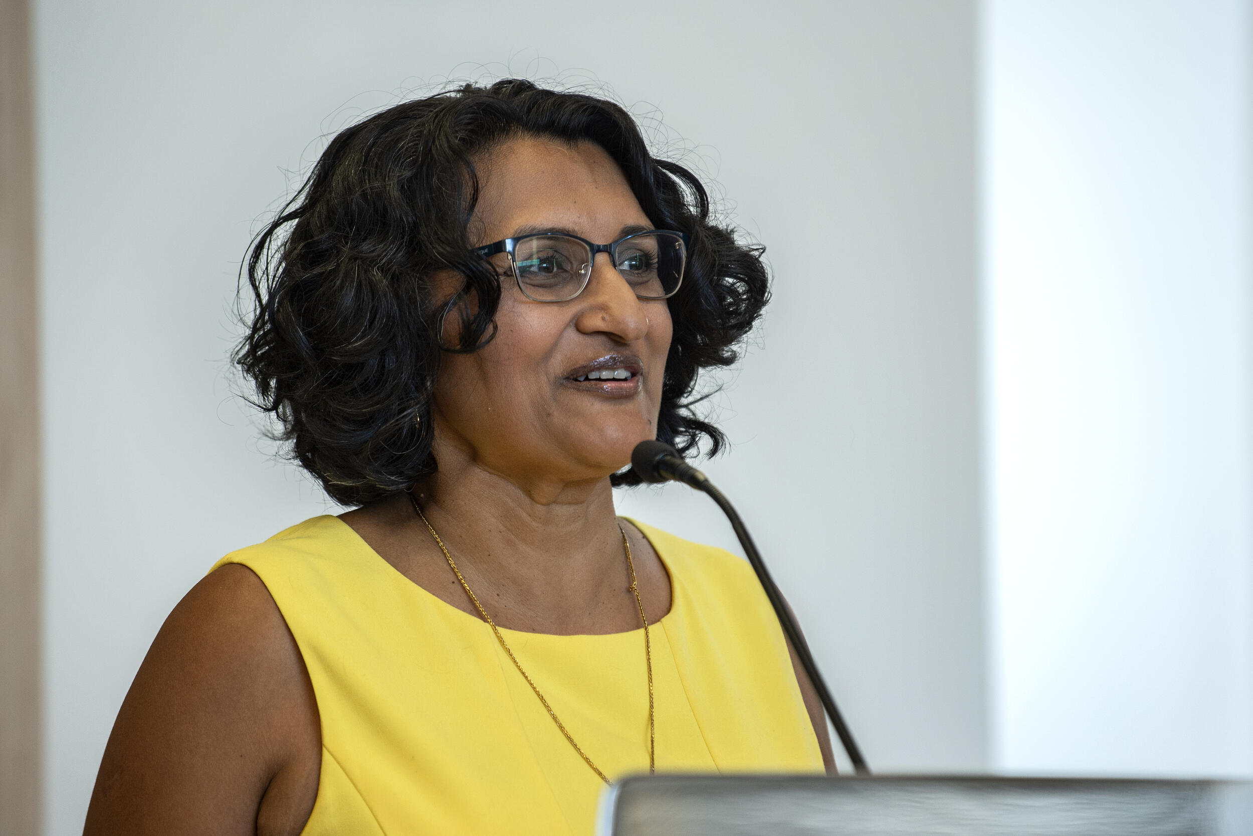 A portrait of Archana A. Pathak, Ph.D. speaking into a microphone on a podium 