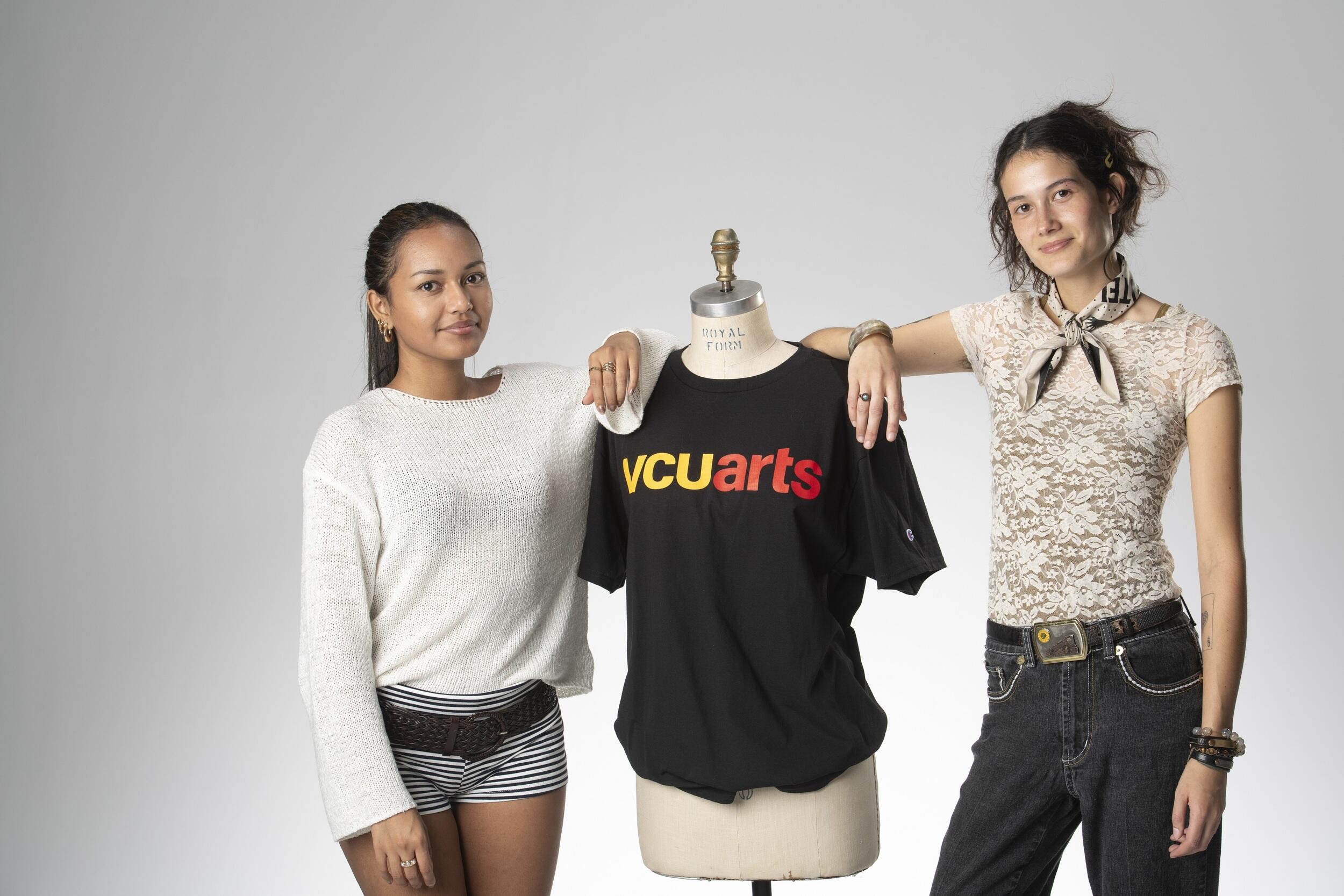 A photo of two women standing on either side of a mannequin wearing a T-shirt that says \"vcuarts\". 