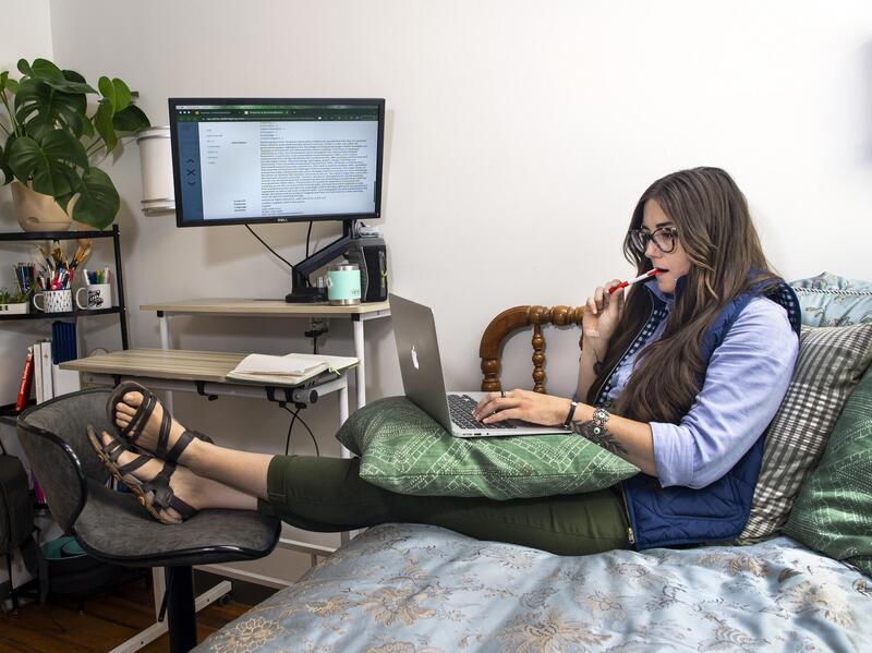 A photo of a woman sitting on a bed with a laptop on her lap. 