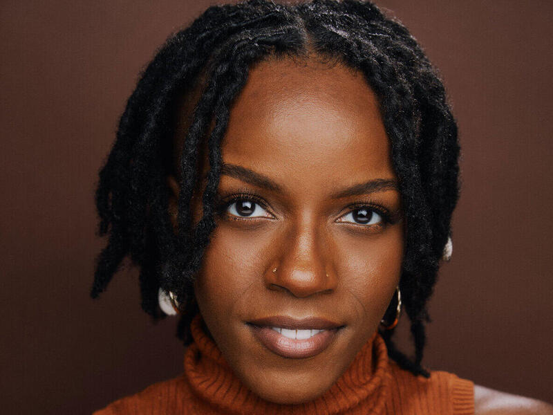 A photo of a woman from the shoulders up. She is wearing a sleeveless turtle neck shirt. 