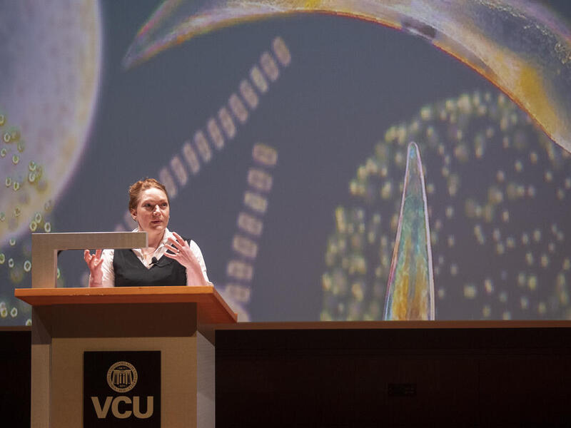A woman at a podium speaking while gesturing her hands in front of her. 