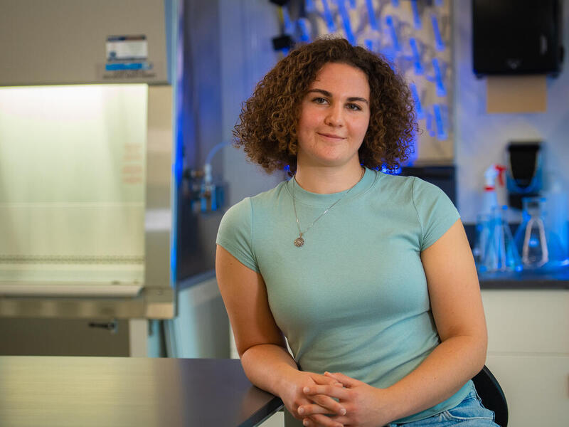 A phot of a woman sitting next to a table. She is leaning her left elbow on the table. 