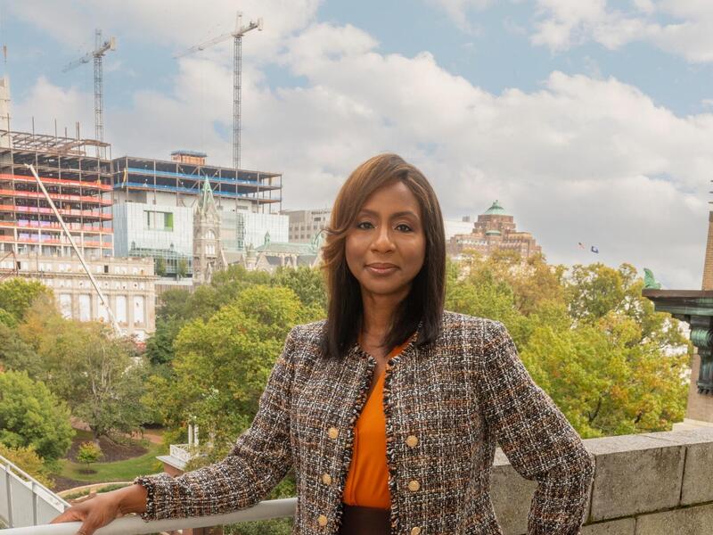 A woman leaning on a railing in front of trees and building construction. 