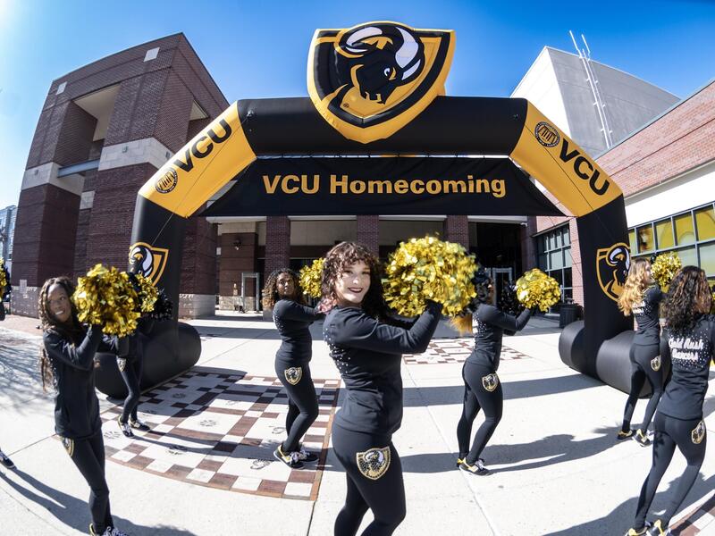 Cheerleaders perform in front of a giant VCU Homecoming sign.