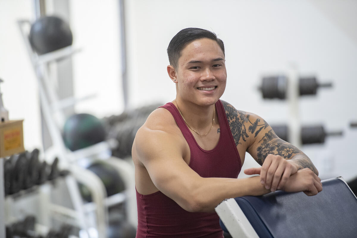 A man wearing a tank top leaning on a piece of exercising equipment. 
