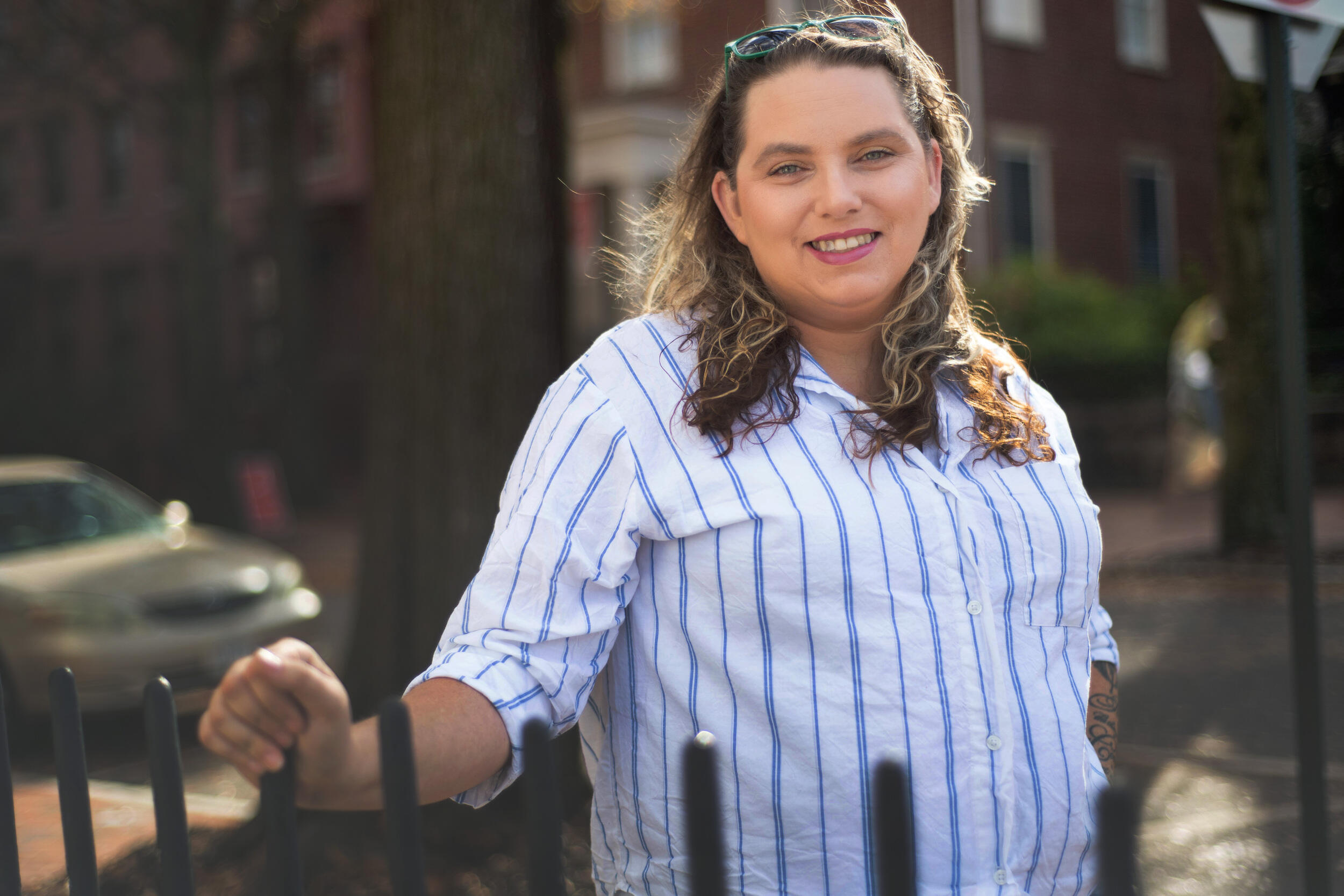 A photo of a woman standing in front of a metal fence. 