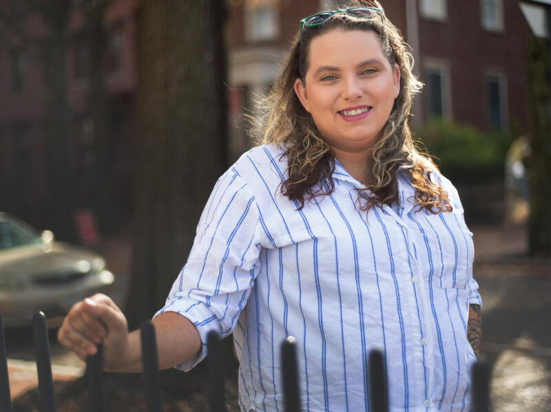 A photo of a woman standing in front of a metal fence. 