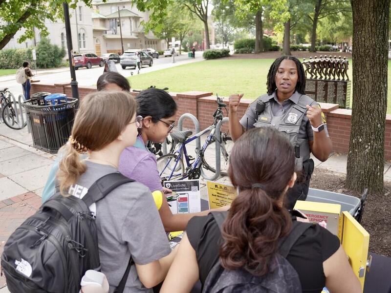 A photo of a police officer talking to four people at a table outside. 