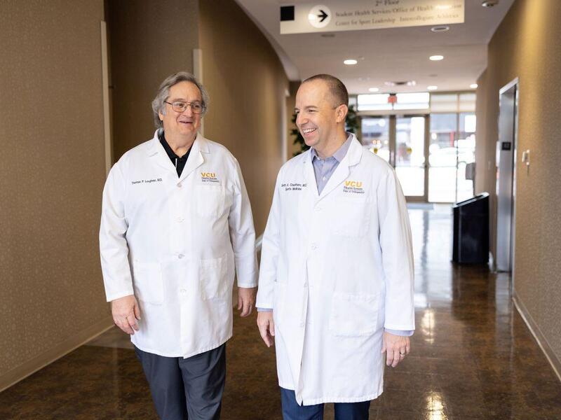 Two men wearing white doctor's coats walking down a hallway. 