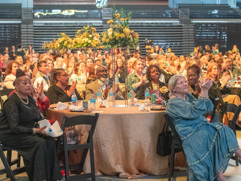 A photo of a room full of people sitting at tables. 