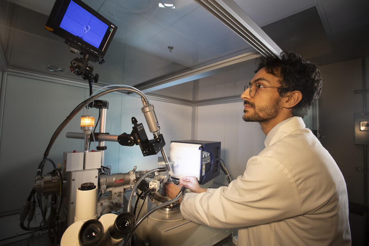 A photo of a man sitting at a table with scienfitic equipment. He's looking up at a screen above him. 