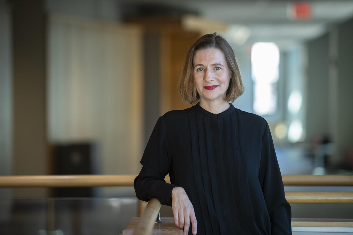 A photo of a woman wearing a black long sleeve shirt leaning against a railing. 