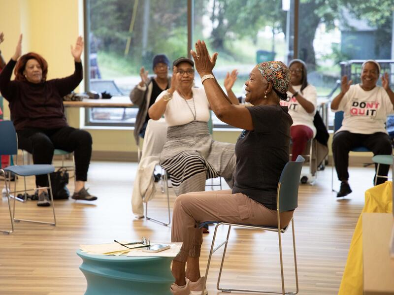 A photo of a room full of women doing chair yoga. 
