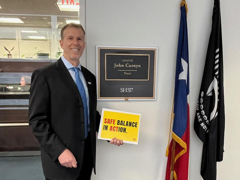 A photo of a mant from the waist up. He is holding a yellow sign that says \"SAFE BALANCE IN ACTION.\"