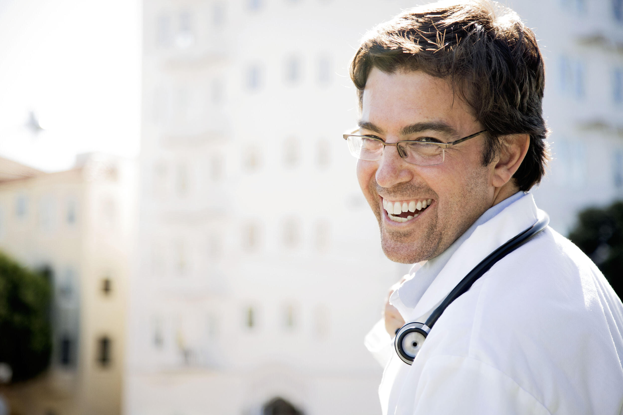 A photo of a man from the shoulders up. He is looking over his right shoulder and smiling. 