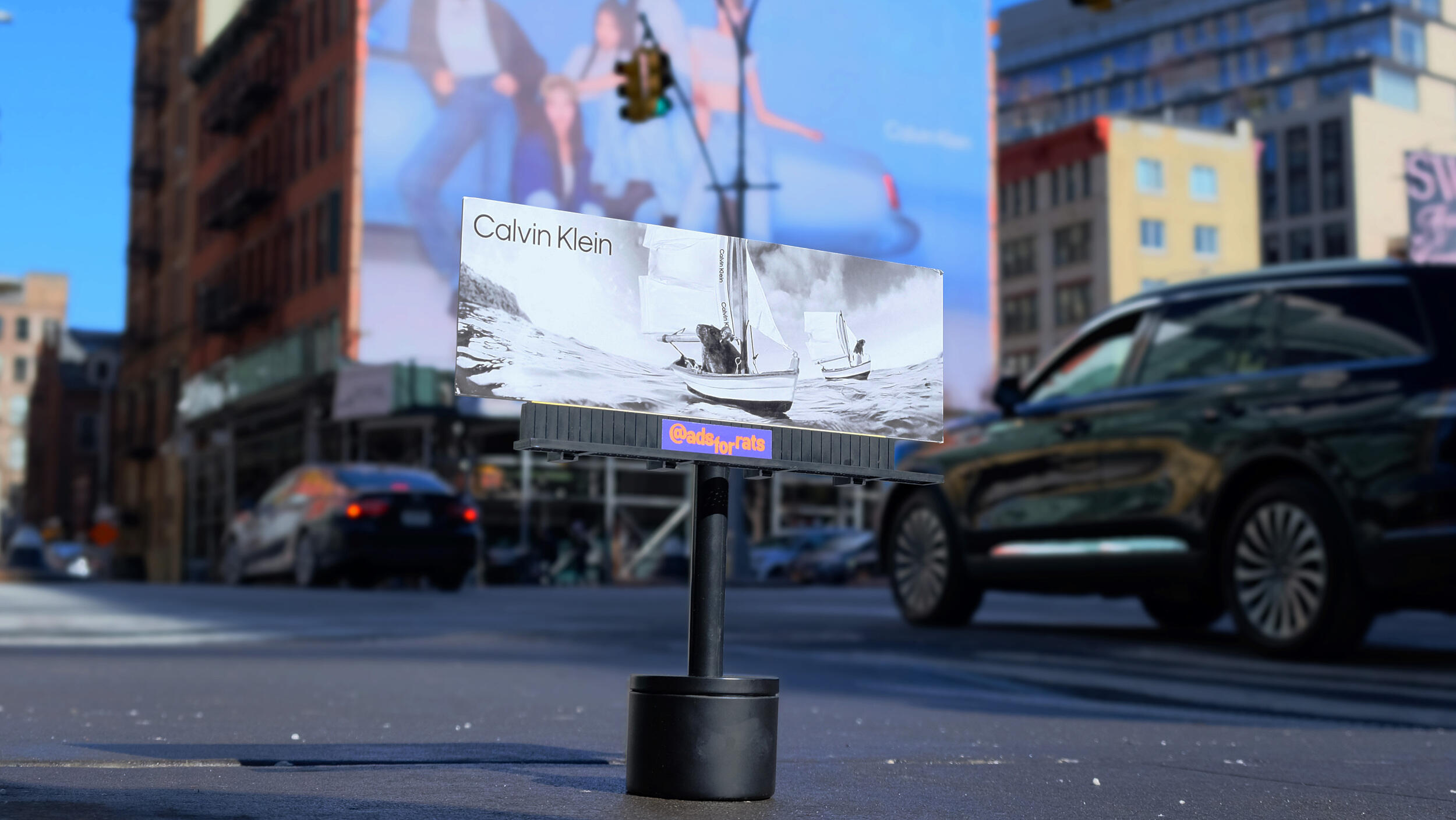 A photo of a mini billboard with an image of a rat on a small sail boat. Black text reads \"Calvin Klein\" 